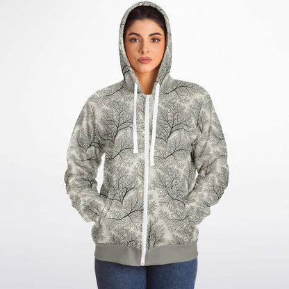 A woman wearing a light gray zip-up hoodie with a black tree branch pattern and white drawstrings, paired with blue jeans, against a plain white background.