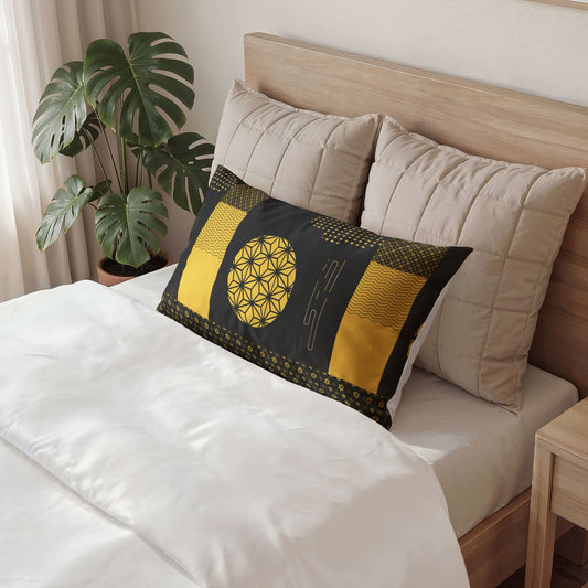 A decorative rectangular pillow with a black and yellow geometric pattern rests on a bed with white linens, beige pillows, and a wooden headboard, with a potted monstera plant in the background.