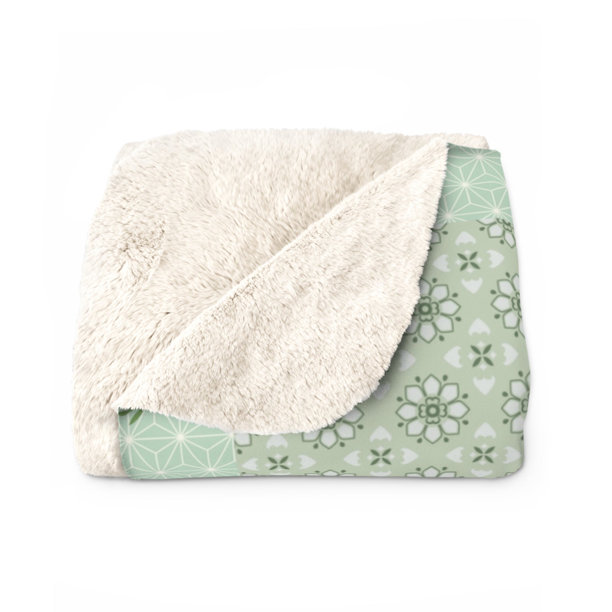 Folded blanket with white sherpa side and green patterned side on a white background