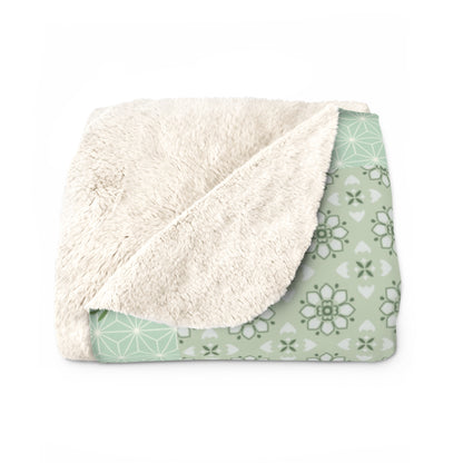 Folded blanket with white sherpa side and green patterned side on a white background