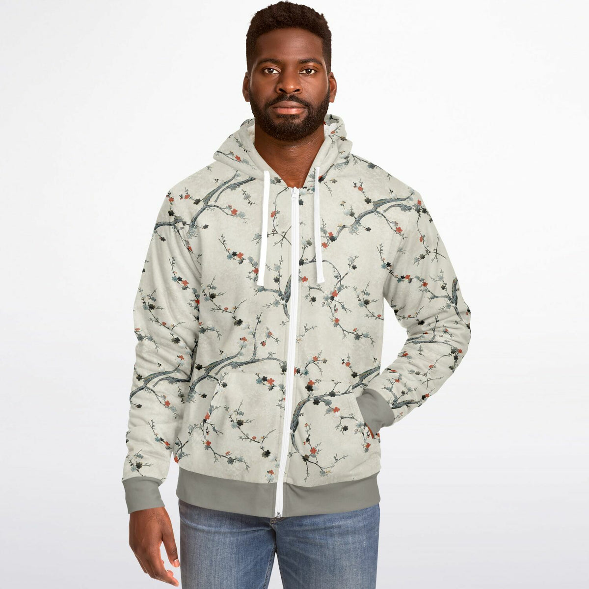 A man wearing a light beige zip-up hoodie with a delicate branch and berry print, paired with blue jeans, against a plain white background.