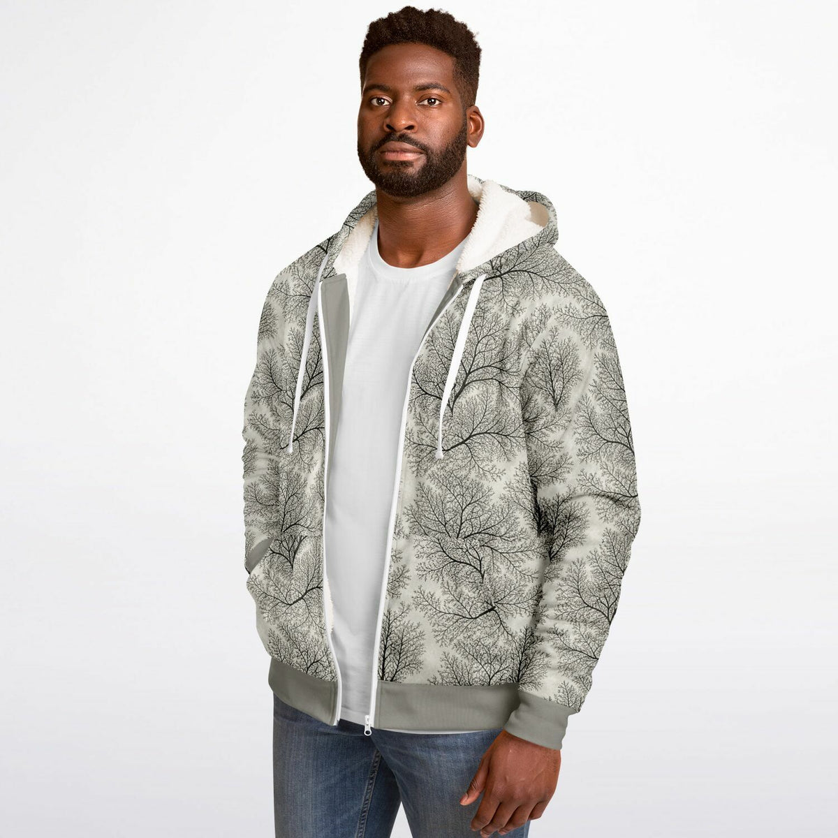 A man wearing a light gray zip-up hoodie with a black tree branch pattern, layered over a white t-shirt and blue jeans, photographed against a plain white studio background.