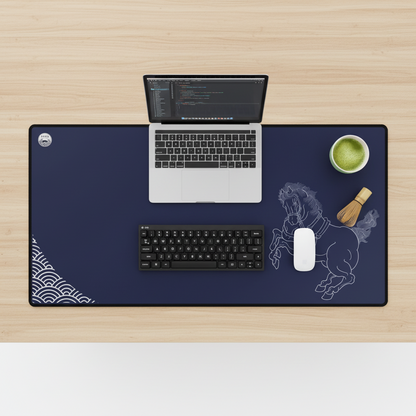 Desk setup with a laptop, keyboard, mouse, and decorative items on a large desk mat.