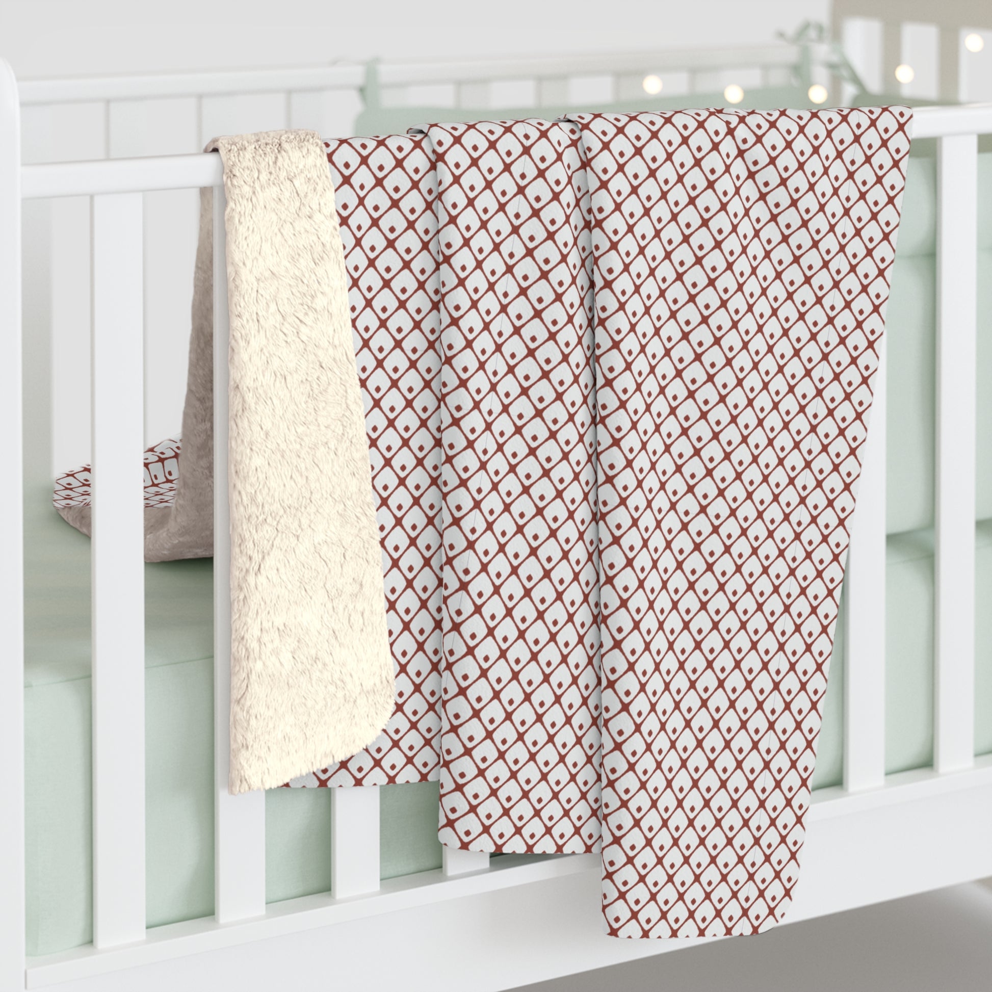 Red and white patterned blanket draped over a white crib