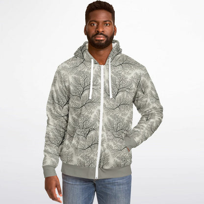 A man wearing a light gray zip-up hoodie with a black tree branch pattern, paired with blue jeans, photographed against a plain white studio background.