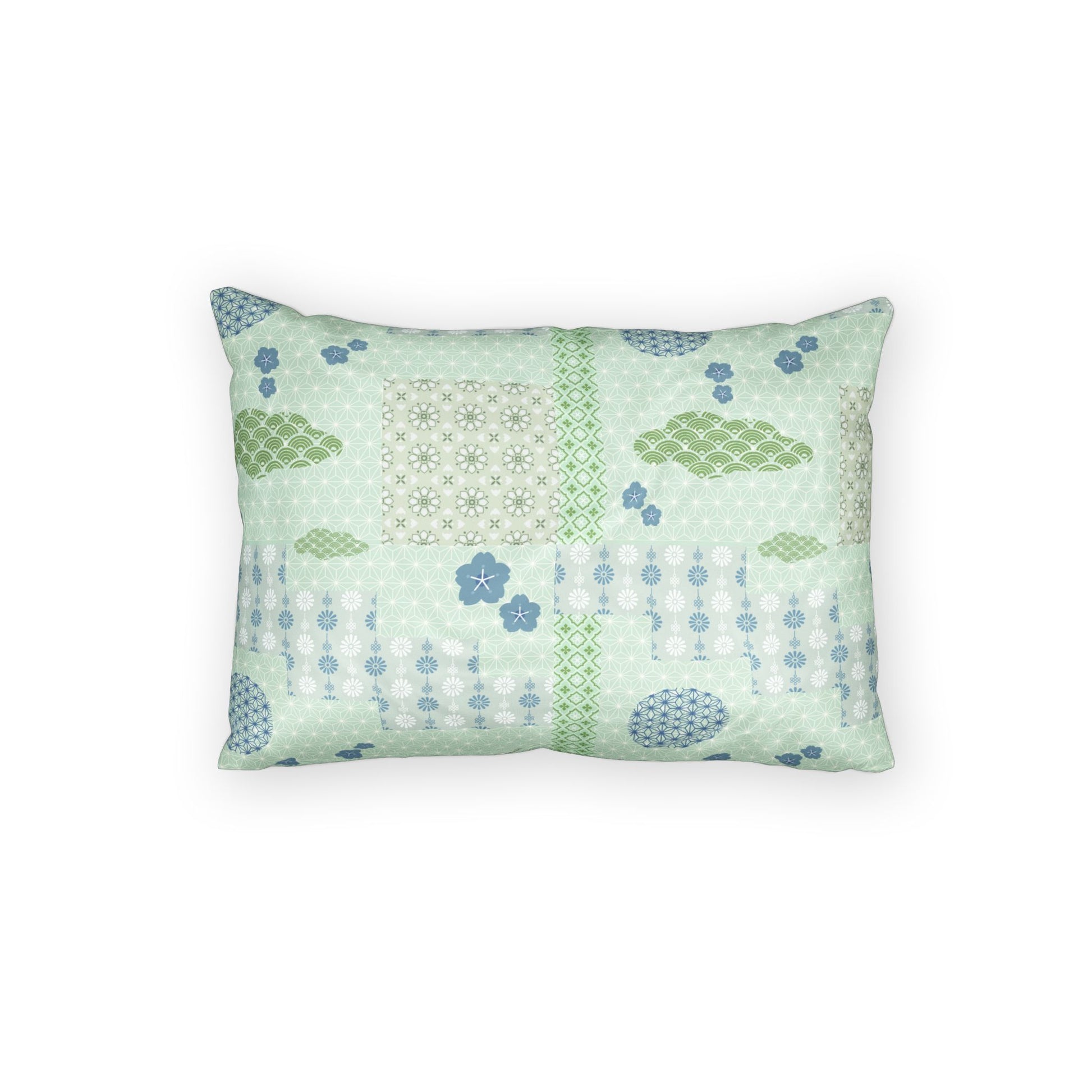 A rectangular decorative throw pillow featuring a patchwork-style print with light green, sage green, and blue patterns, including geometric grids, floral motifs, and dotted lines, set against a plain white background.