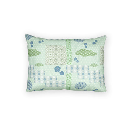 A rectangular decorative throw pillow featuring a patchwork-style print with light green, sage green, and blue patterns, including geometric grids, floral motifs, and dotted lines, set against a plain white background.
