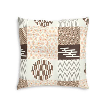 A square decorative throw pillow featuring a patchwork design of geometric and ikat-inspired patterns in brown, beige, and orange on an off-white background.