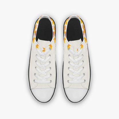 A pair of low-top canvas sneakers shown from a top-down view. The shoes feature an off-white canvas upper with a black rubber toe cap and sole edge, white laces, and a yellow and orange flame pattern printed around the collar.