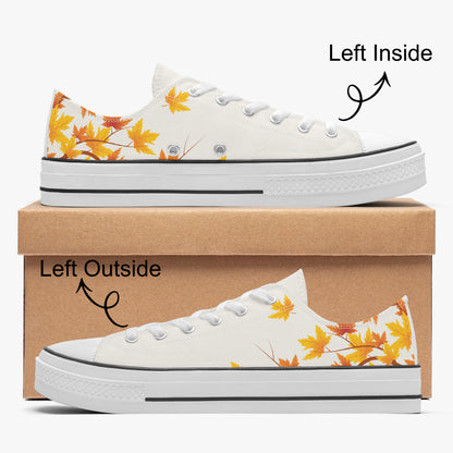 A pair of low-top canvas sneakers shown from both left inside and left outside views, stacked on a brown shoebox against a light gray background. The shoes are white with a yellow and orange autumn leaf pattern on the heel and side.
