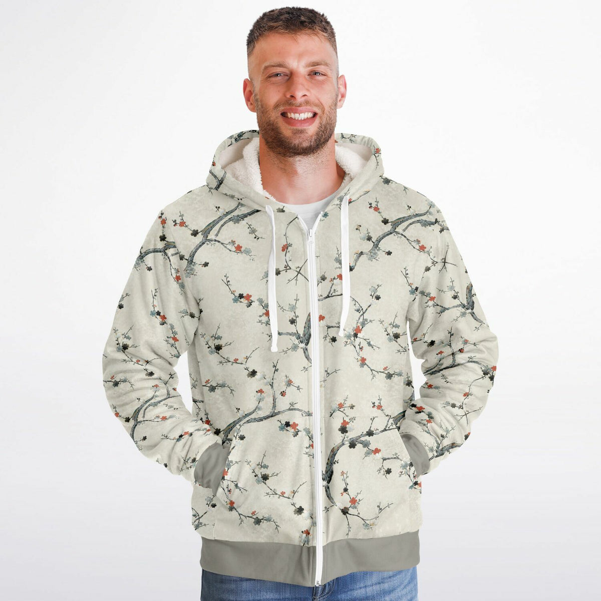 A man wearing a light beige zip-up hoodie with a detailed branch and blossom print in black, gray, and muted red, set against a plain white background.
