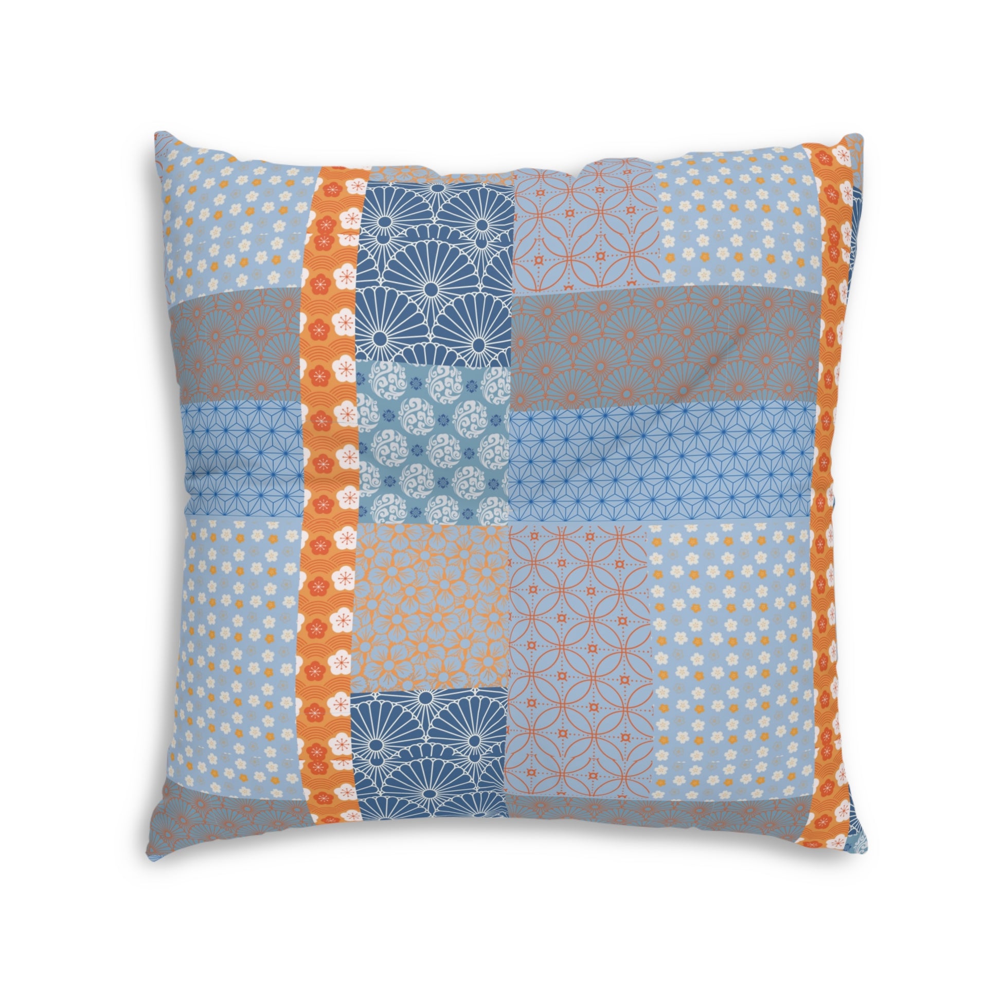 A square decorative throw pillow featuring a patchwork quilt design with various blue, orange, and gray geometric and floral patterns, set against a plain white background.