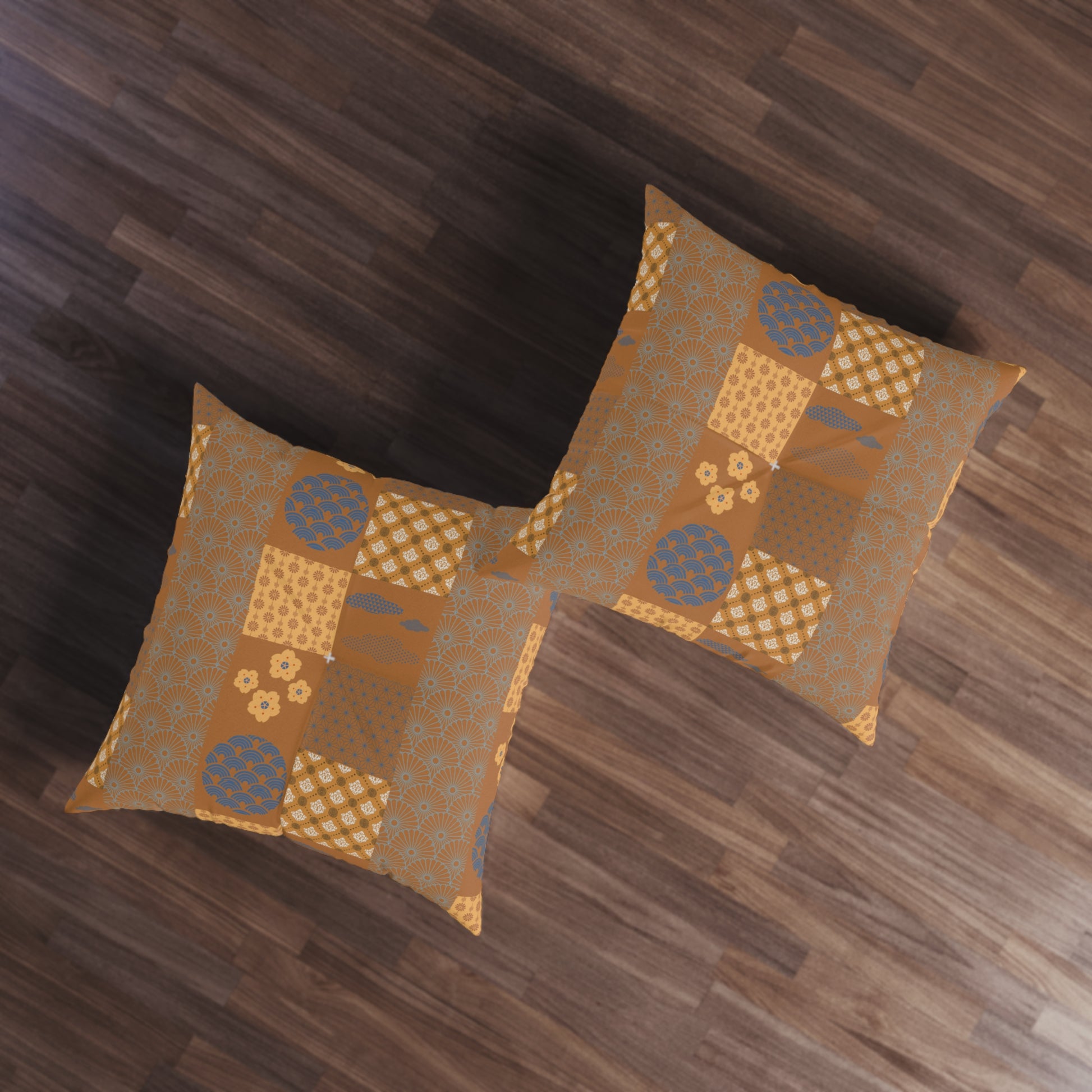 Two square decorative throw pillows with a patchwork pattern in shades of brown, gold, and blue, displayed on a dark wood floor.