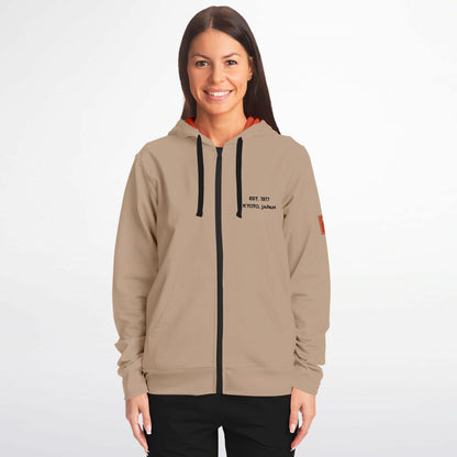A woman modeling a beige zip-up hoodie with black drawstrings, a black front zipper, and black text on the left chest reading 'EST. 1997 KANSAS CITY, MO'.