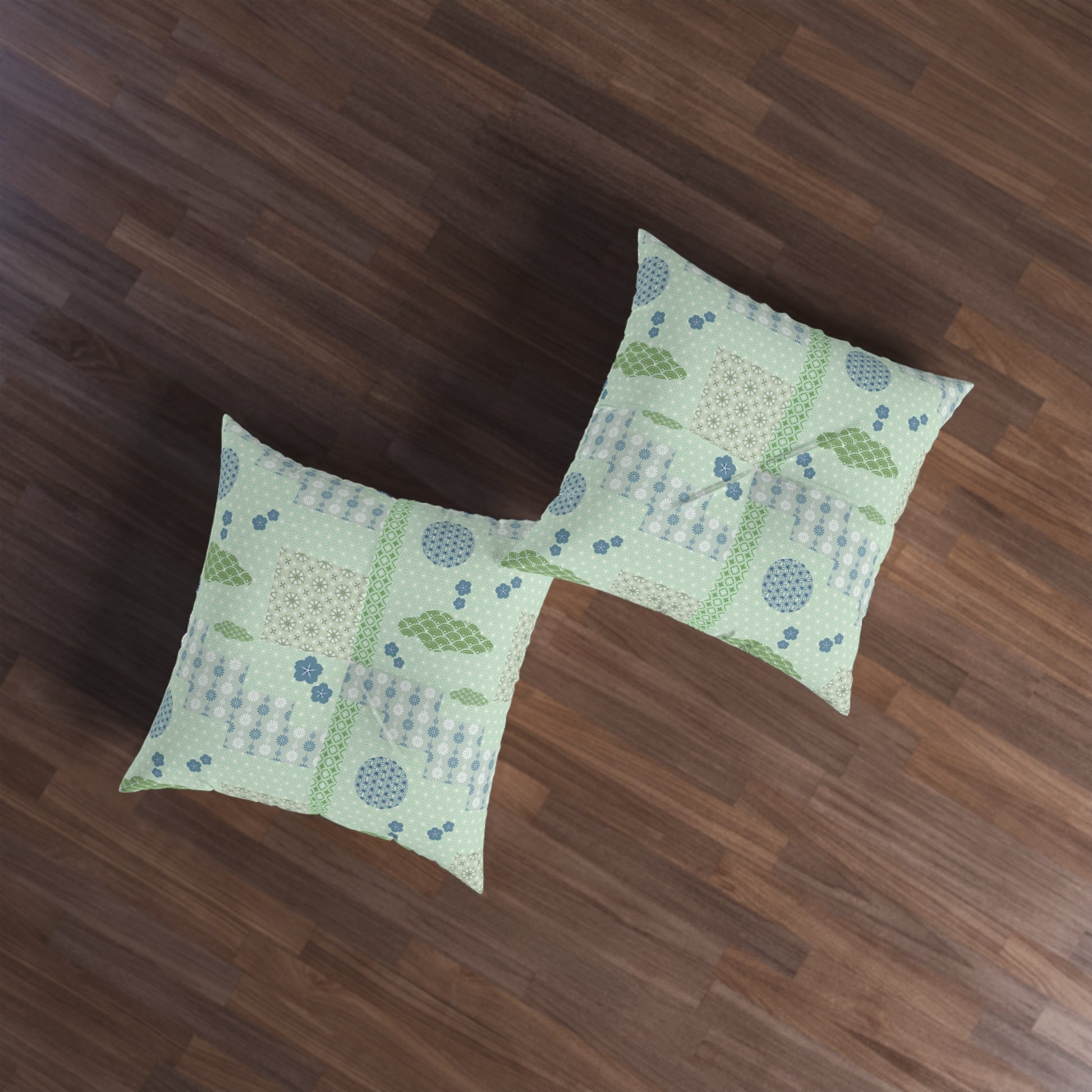 Two square decorative throw pillows with a light green patchwork pattern featuring blue dots, green leaves, and beige geometric blocks, displayed on a dark brown wooden floor.