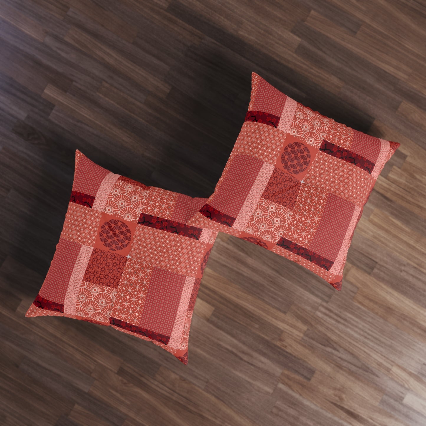 Two square decorative throw pillows with a red and orange patchwork quilted pattern, displayed on a dark wood floor.