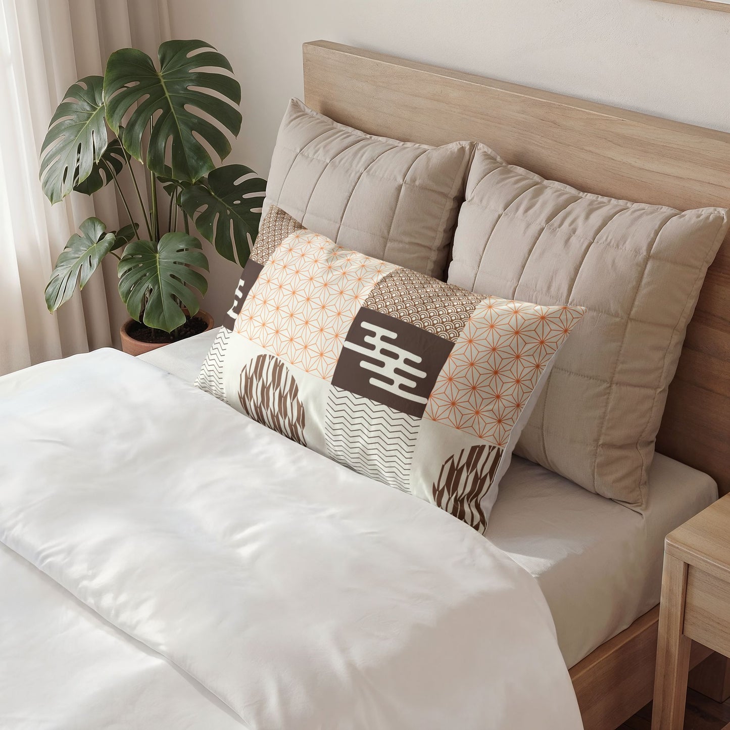 A styled bedroom scene showing a bed with white bedding, large beige pillows, and a decorative rectangular accent pillow with patchwork patterns in beige, brown, white, and orange. A wooden headboard, side table, and potted monstera plant are visible.