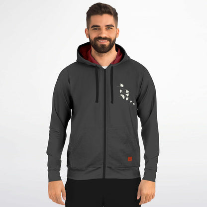 A man wearing a dark gray zip-up hoodie with a black drawstring, a white graphic print on the left chest, and a red-lined hood, standing against a light gray background.