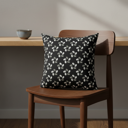 Decorative pillow with leaf pattern on a wooden chair against a neutral wall.
