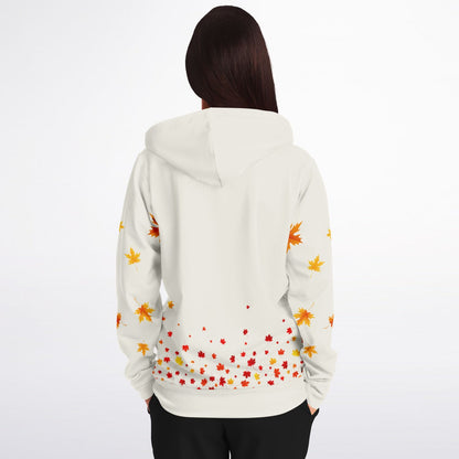 A woman viewed from behind wearing a white hoodie with a colorful autumn leaf pattern on the back and sleeves, paired with black pants, against a plain white background.