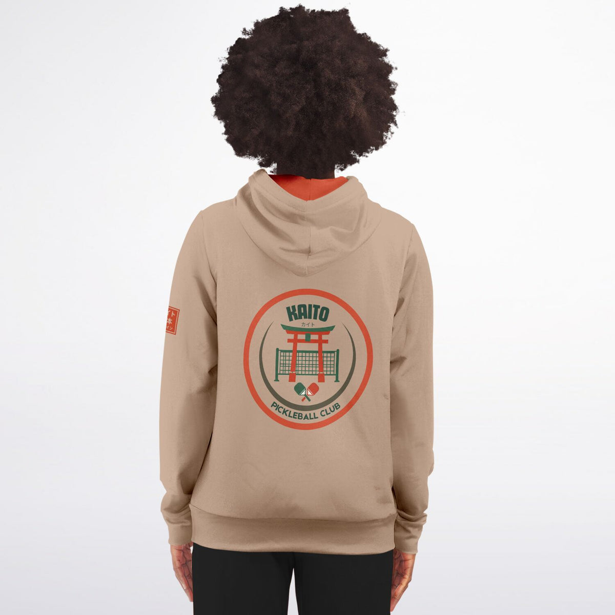 A person shown from the back wearing a beige hoodie with a large circular 'Kaito Volleyball Club' graphic on the back and a small orange patch on the sleeve, against a plain light gray studio background.