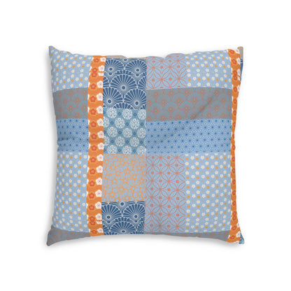 A square decorative throw pillow featuring a patchwork quilt design with various blue, gray, and orange patterns, set against a plain white background.