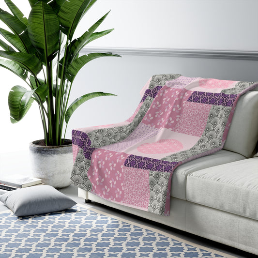 Pink and purple patchwork blanket on a white sofa with a plant and rug in the background