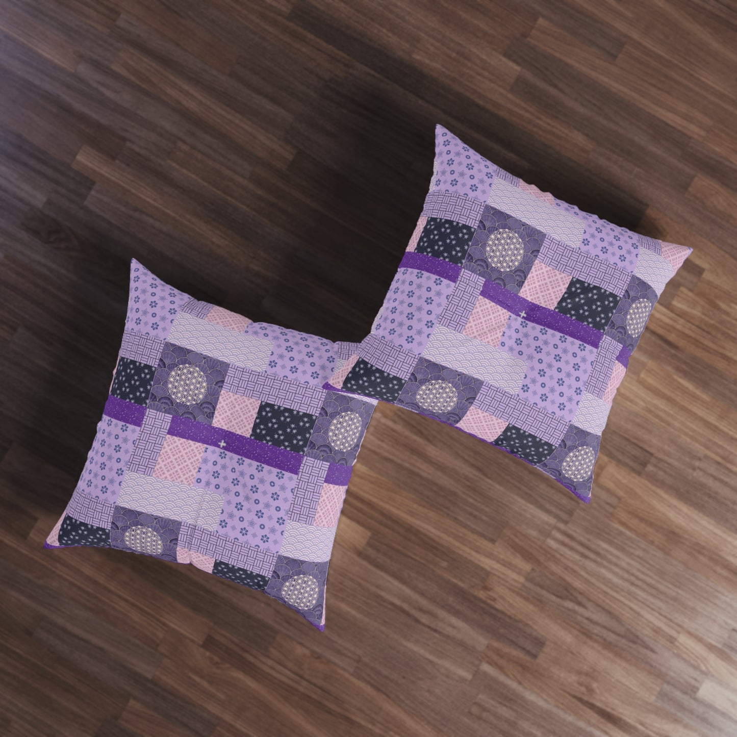 Two square patchwork throw pillows in shades of purple, pink, and black with geometric patterns, arranged on a dark brown wooden floor.
