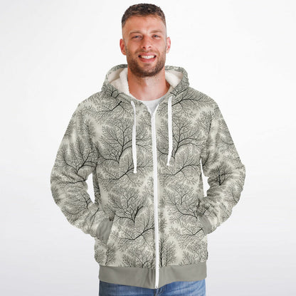 A man wearing a zip-up hoodie with an all-over tree branch pattern in black and gray on a light gray background, paired with blue jeans, against a plain white studio backdrop.