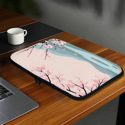 Laptop sleeve with cherry blossom design on a wooden desk with a laptop and mug.