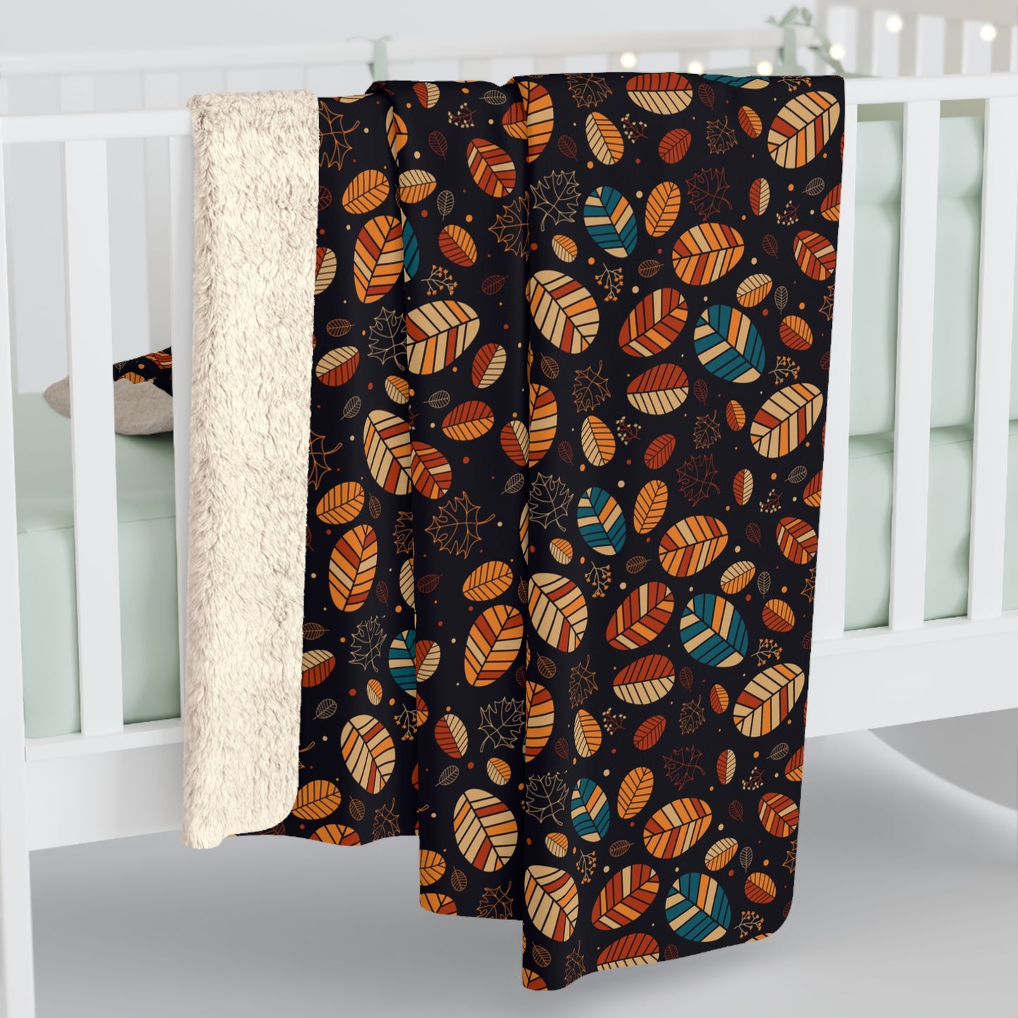 A baby blanket draped over a white crib, featuring a black background with a colorful pattern of stylized leaves in orange, teal, and brown, with a soft cream sherpa lining visible on the left.