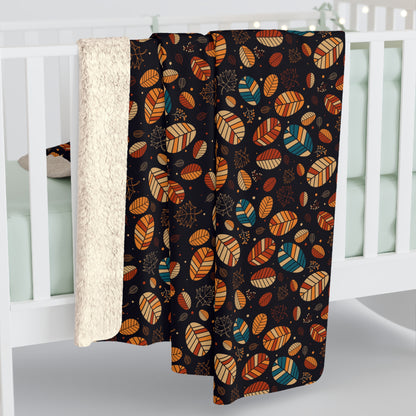 A baby blanket draped over a white crib, featuring a black background with a colorful pattern of stylized leaves in orange, teal, and brown, with a soft cream sherpa lining visible on the left.