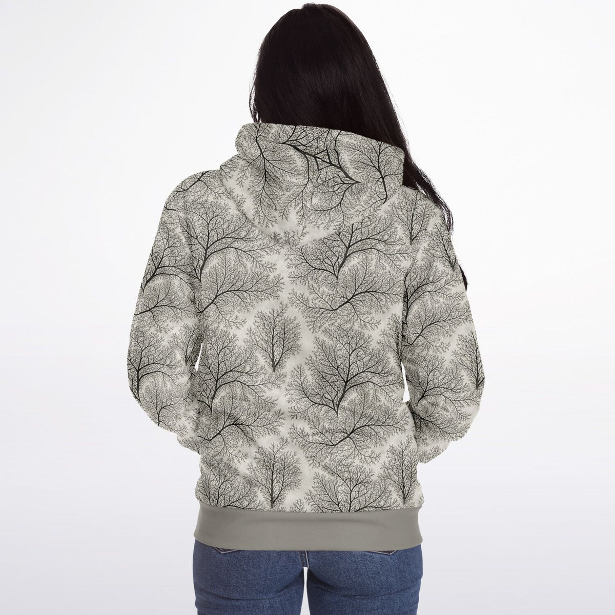 A woman viewed from behind wearing a hooded sweatshirt with an all-over abstract tree branch pattern in black and gray on a light gray background, paired with blue jeans against a plain white studio backdrop.
