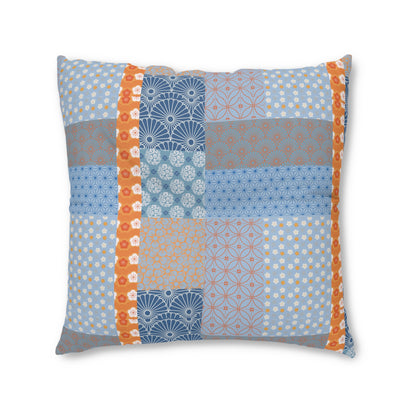 A square decorative throw pillow featuring a patchwork design of various blue, gray, and orange patterns, set against a plain white background.