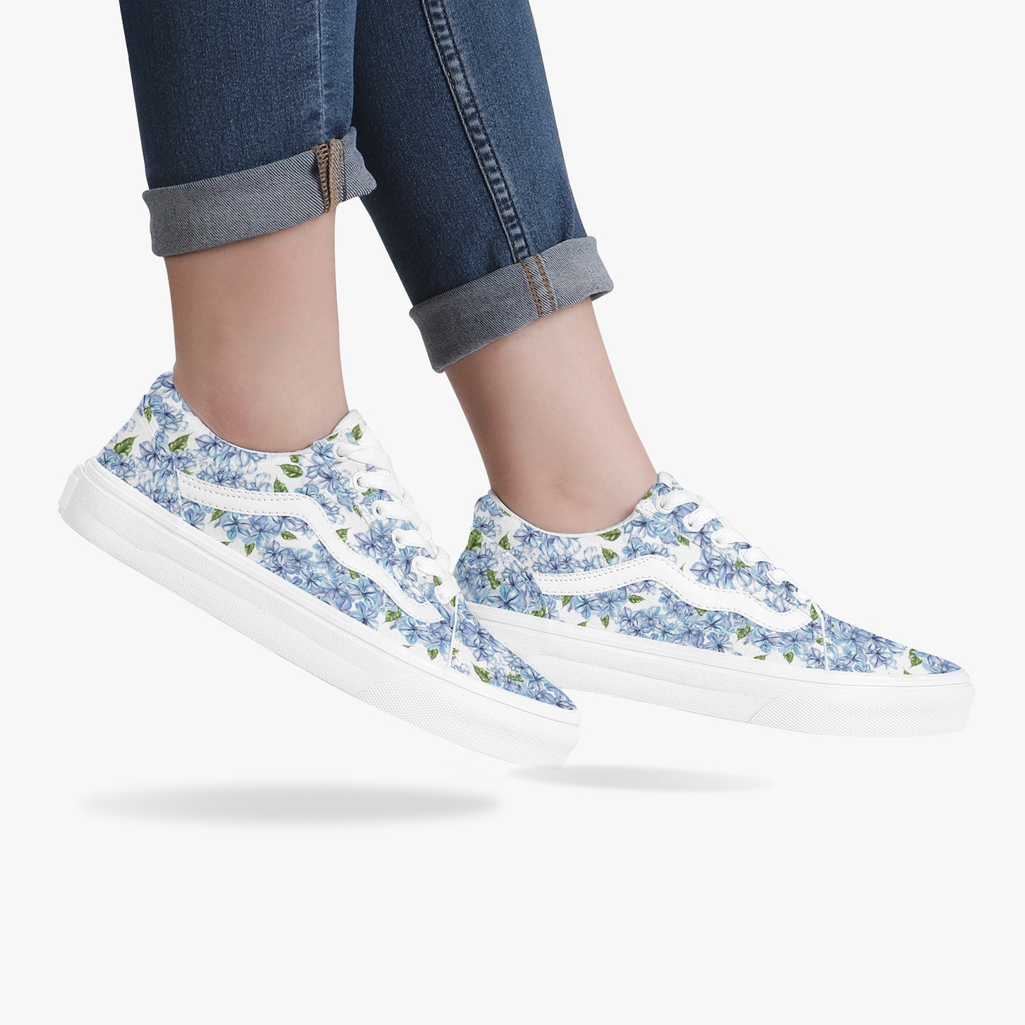 White sneakers with blue floral pattern worn with rolled-up jeans on a white background