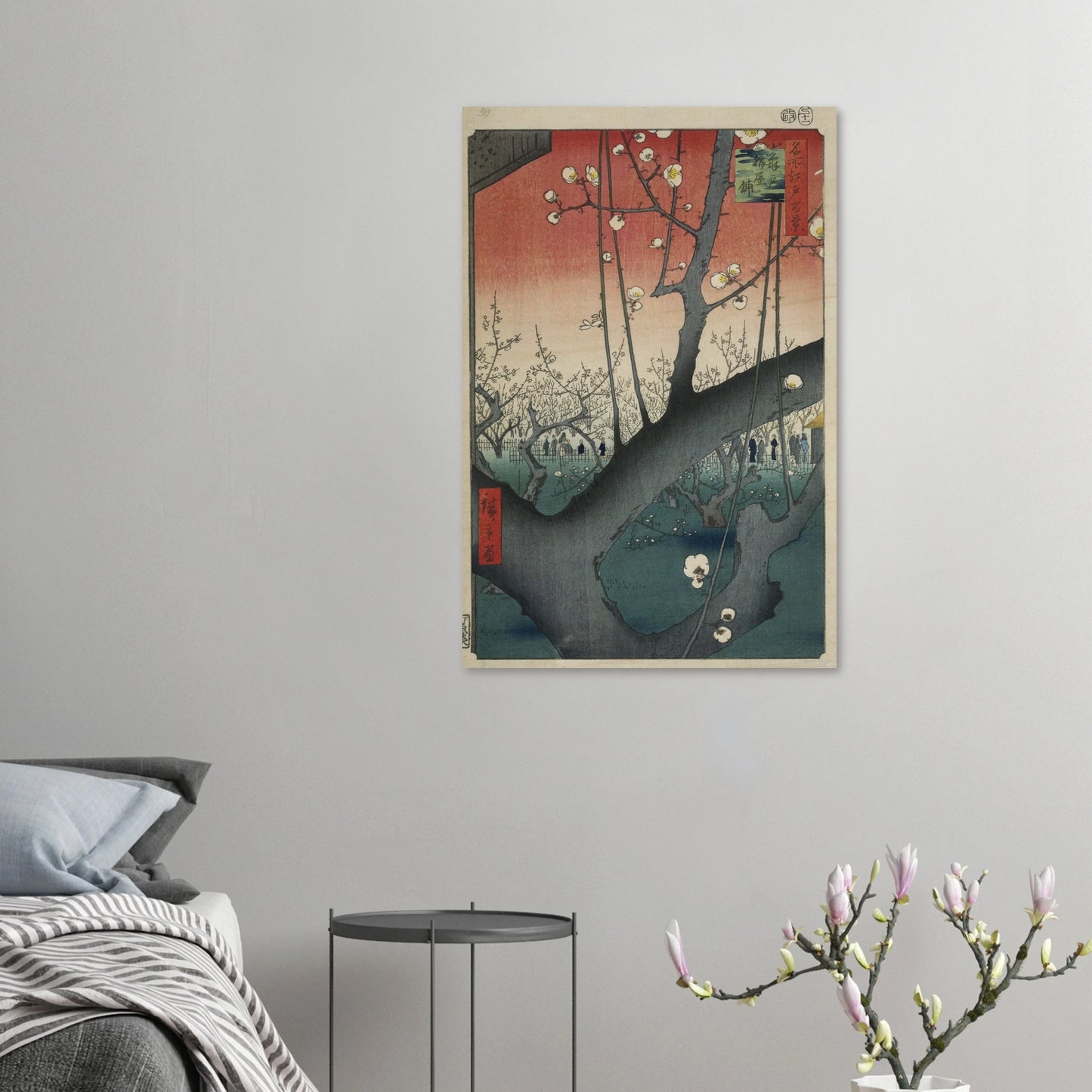 Framed artwork on a wall above a bed with a side table and decorative branch.