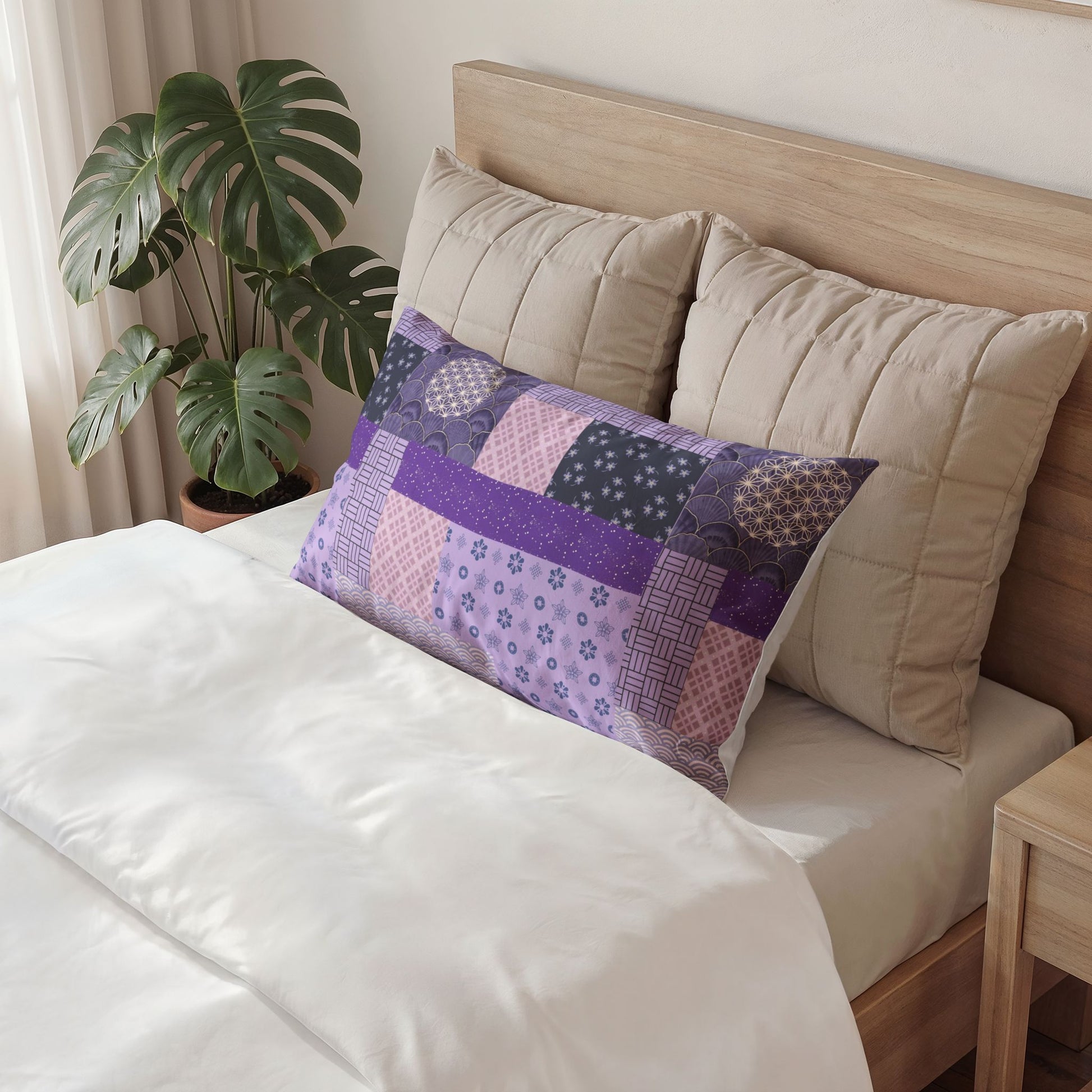 A rectangular patchwork pillow in shades of purple, pink, and navy with floral and geometric patterns, styled on a bed with beige pillows and white bedding next to a green plant.