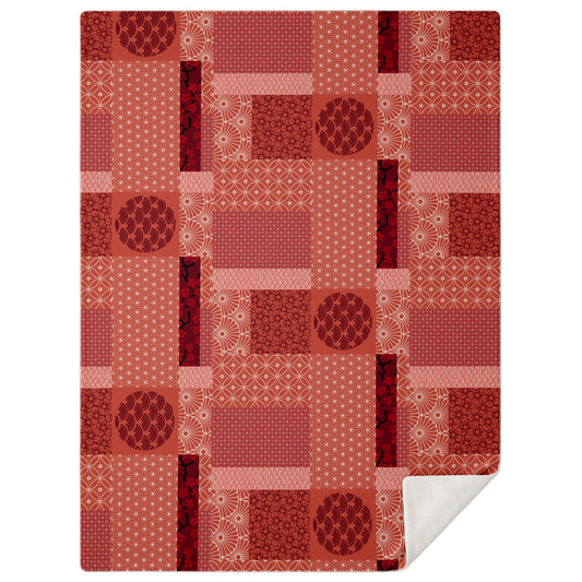 A high-angle, square photograph of a minimalist bedroom featuring a bed made of dark walnut wood. Draped across the bed is the Japanese Red Rising Sun Patchwork Blanket from Kaito Japan Design. The blanket is a monochromatic masterpiece in rich, varying shades of red, featuring a central rising sun motif surrounded by a patchwork of traditional Wagara patterns like Seigaiha waves and Kikko tortoise shells. Natural morning light streams through the window, highlighting the depth of the red palette and creati