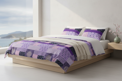 A bed dressed in a purple and lavender patchwork quilt and matching pillow shams, styled in a bright, modern bedroom with a wooden platform bed frame and a window overlooking water.