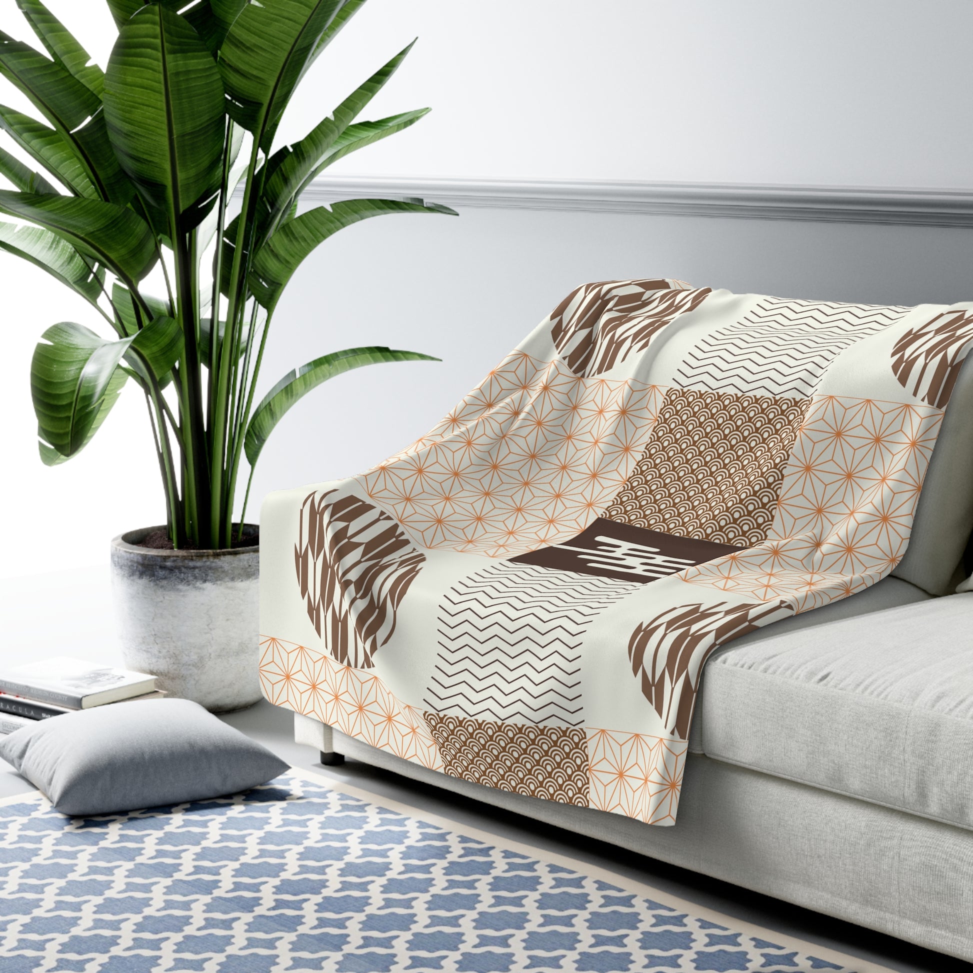 Patterned blanket draped over a sofa with a plant and rug in the background