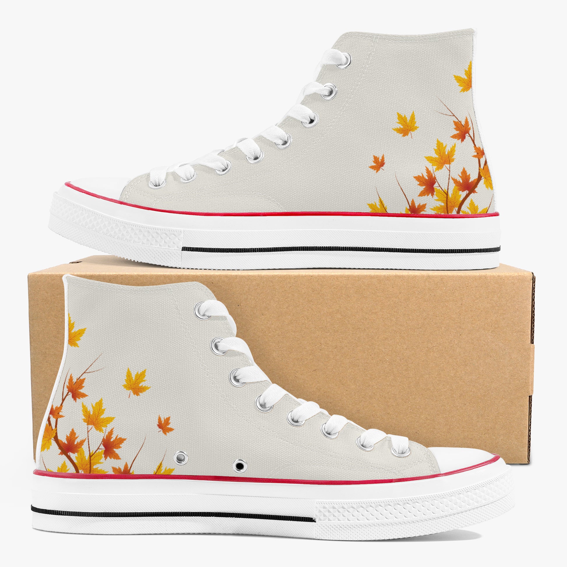 A pair of high-top canvas sneakers in light gray, decorated with orange and yellow maple leaves near the heel. One shoe is displayed on top of a brown cardboard box, and the other is positioned in front.