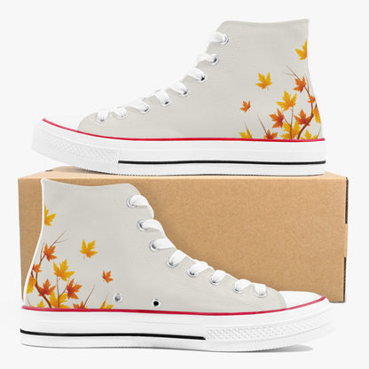 A pair of high-top canvas sneakers in light gray, decorated with orange and yellow maple leaves near the heel. One shoe is displayed on top of a brown cardboard box, and the other is positioned in front.