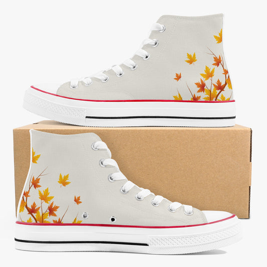 A pair of high-top canvas sneakers in light gray, decorated with orange and yellow maple leaves near the heel. One shoe is displayed on top of a brown cardboard box, and the other is positioned in front.