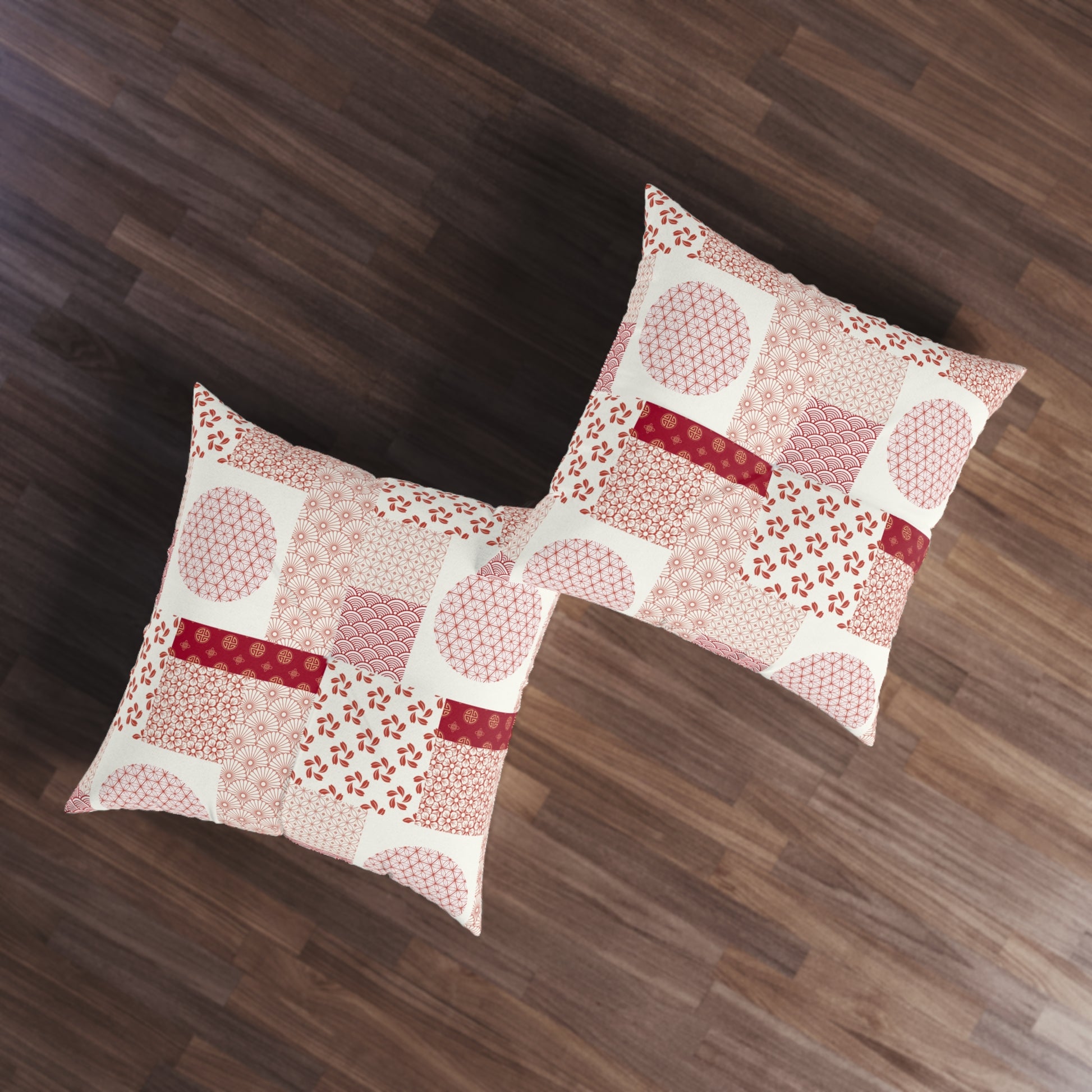 Two square decorative throw pillows with a patchwork print in pink, red, and white, arranged on a dark brown wooden floor.