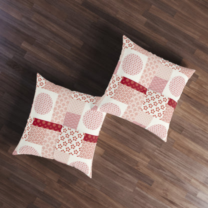 Two square decorative throw pillows with a patchwork print in pink, red, and white, arranged on a dark brown wooden floor.