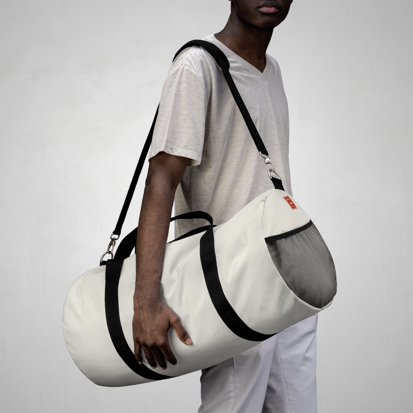 Person holding a white duffel bag with black straps on a plain background