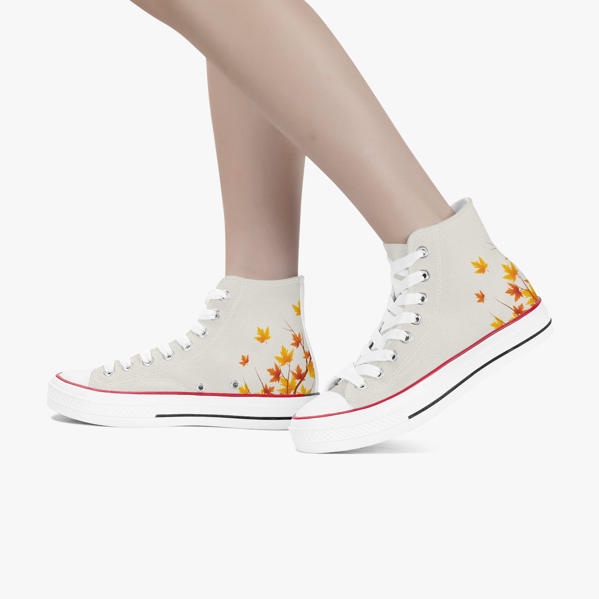 A pair of high-top canvas sneakers in off-white, decorated with a yellow and orange autumn leaf pattern on the sides, shown on a model's feet against a light gray background.