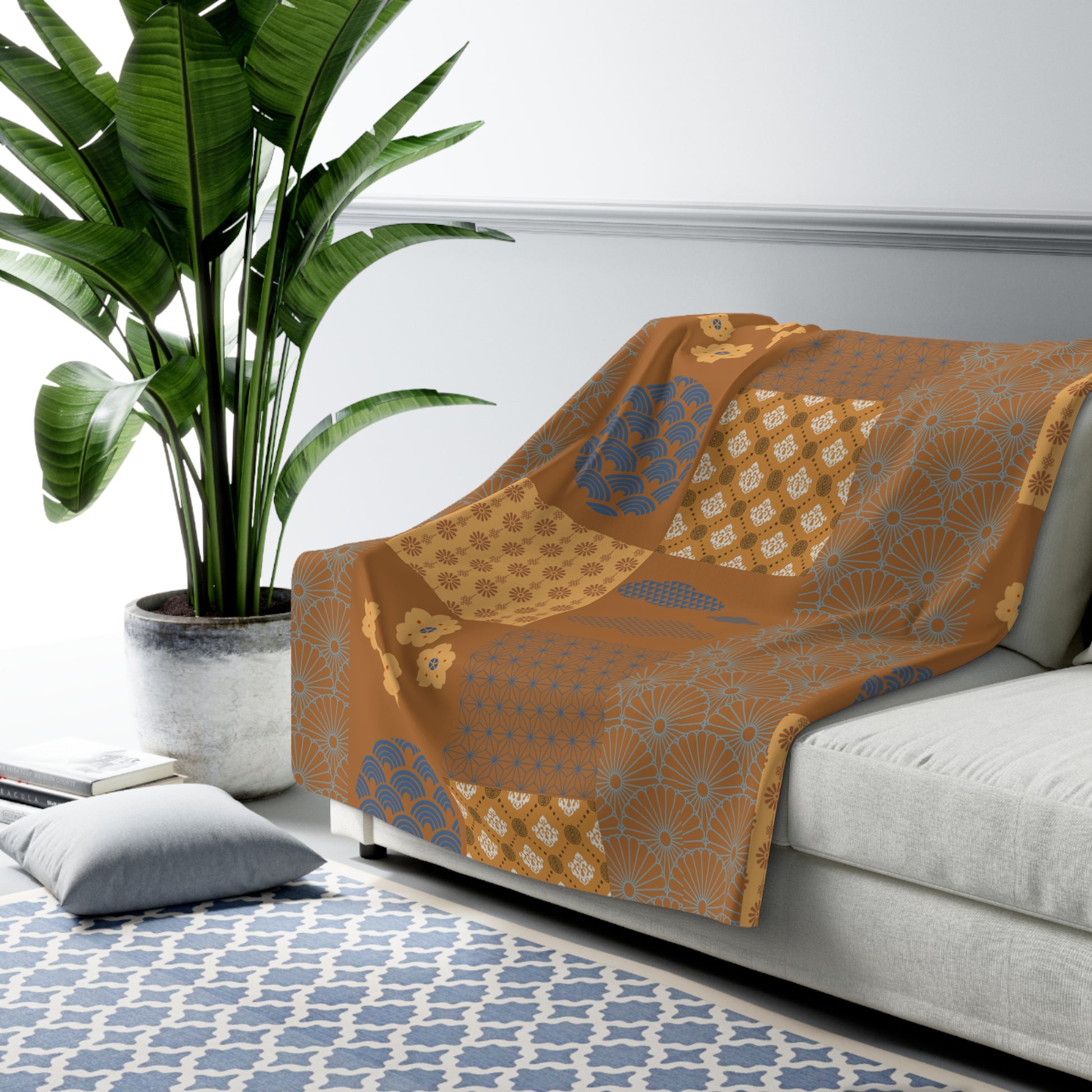 Patterned orange blanket draped over a gray sofa with a plant and rug in the background