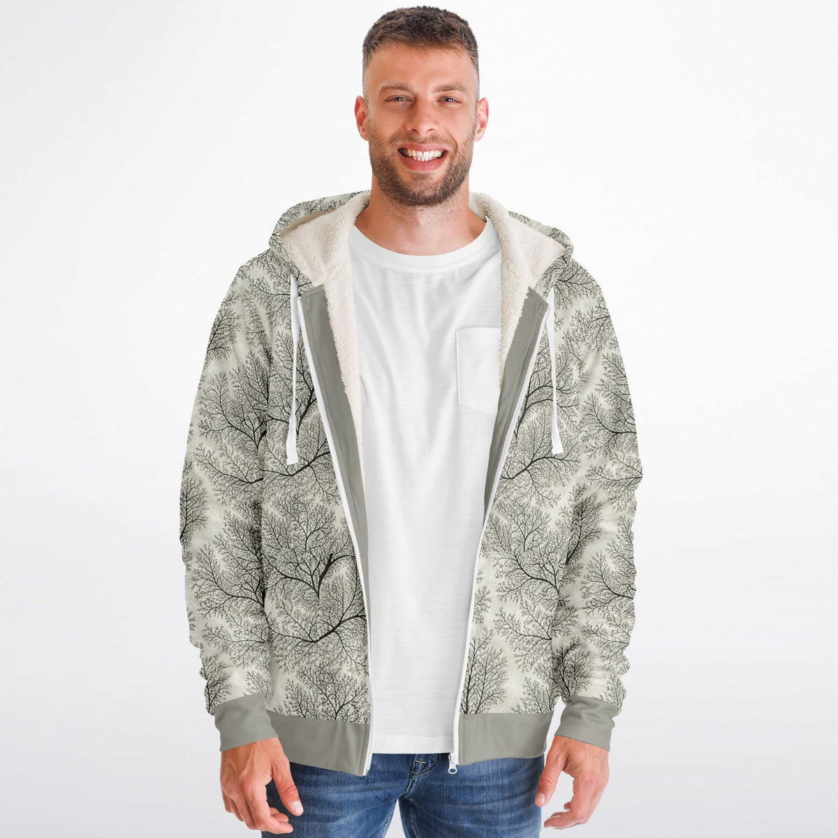 A man wearing a zip-up hoodie with a gray and white tree branch pattern, layered over a white t-shirt and blue jeans, against a plain white background.