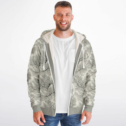 A man wearing a zip-up hoodie with a gray and white tree branch pattern, layered over a white t-shirt and blue jeans, against a plain white background.